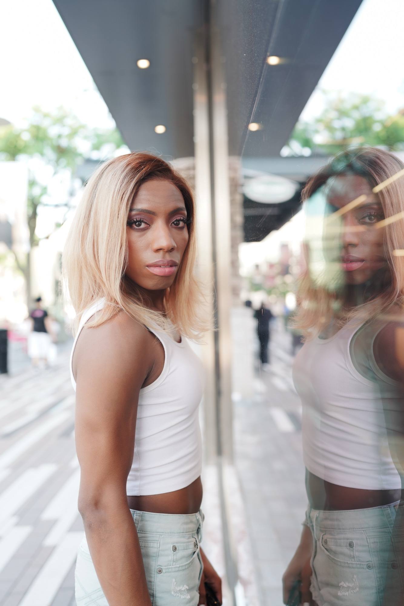 Editorial street portrait of a woman in a white top, mirrored in a storefront window