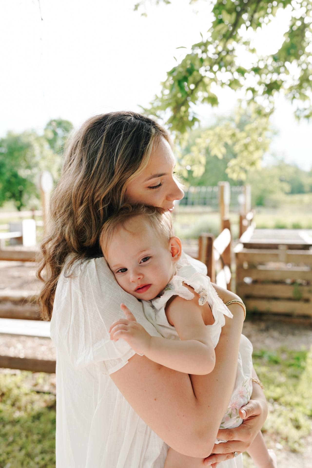 Mother cradling her baby beneath a tree in soft summer light